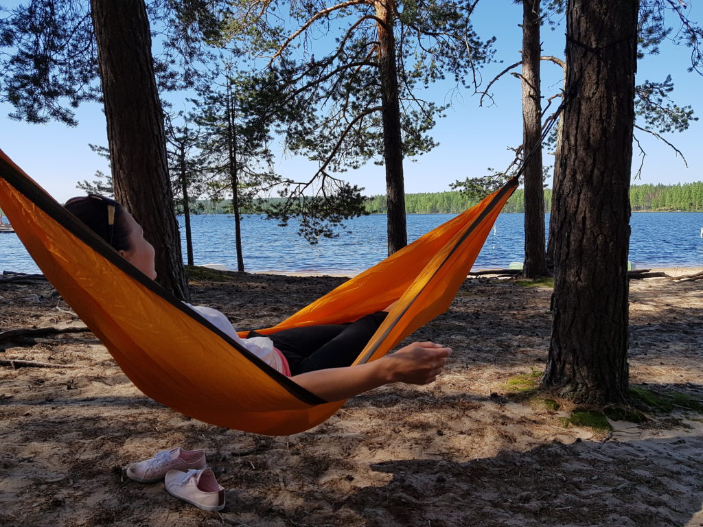 Nainen makaa rennosti riippukeinussa rannalla.