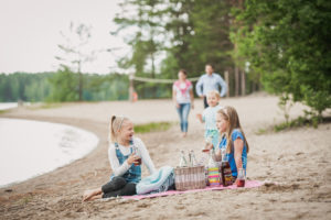 Tytöt istuvat Piispalan rannalla viltin päällä