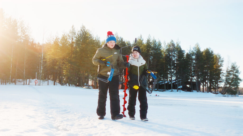 Kaksi nuorta kävelevät jäälle kairan ja pilkkien kanssa.