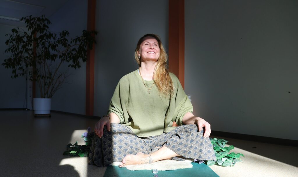 Nainen istuu auringon valokeilassa Piispalassa joogamatolla.