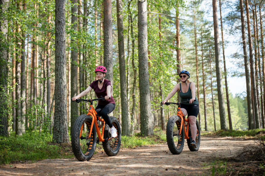 Nainen ja nuori pyöräilevät Piispalan mäntymetsässä.