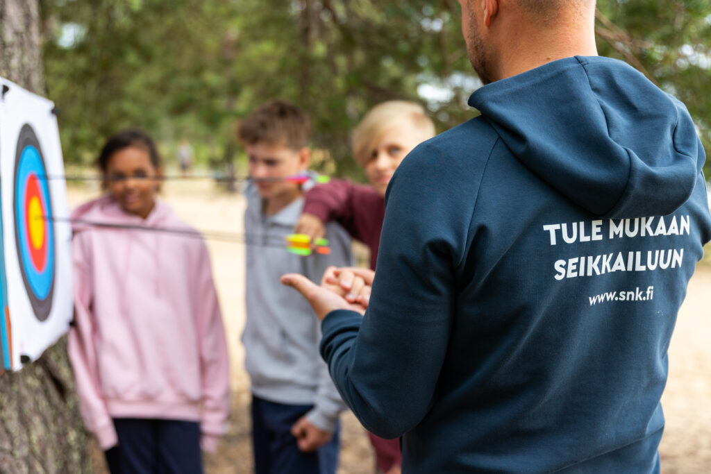 Piispalan työntekijä neuvoo nuoria jousiammunnassa.
