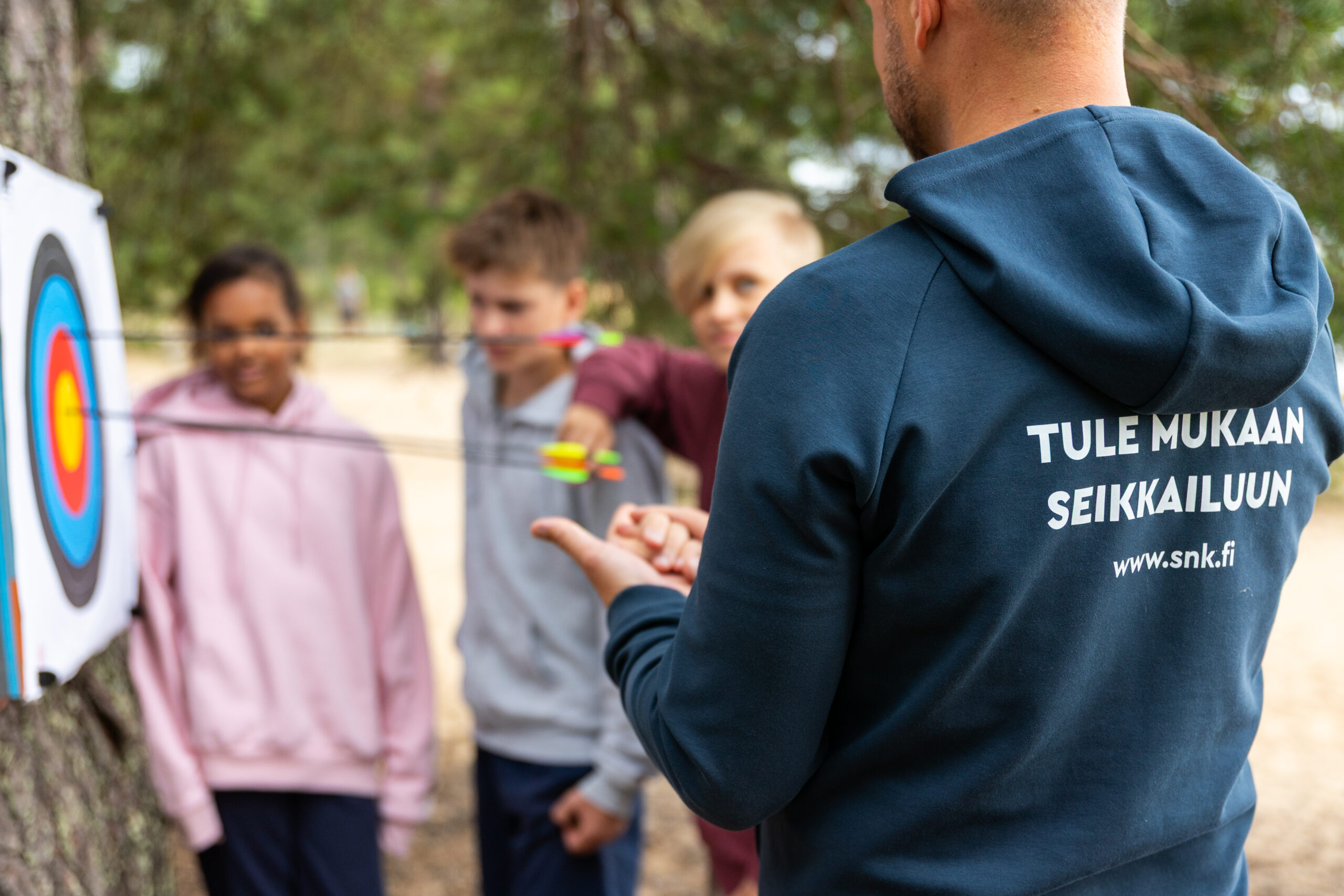 Piispalan työntekijä neuvoo nuoria jousiammunnassa.