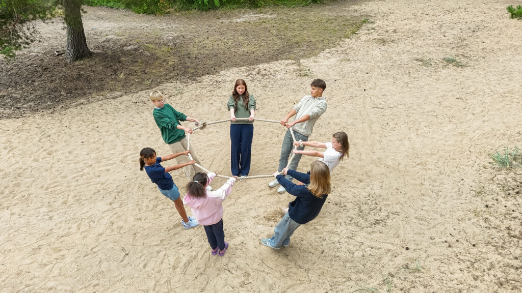 Ryhmä nuoria seisoo hiekkarannalla ja pitelevät yhdessä köyttä.