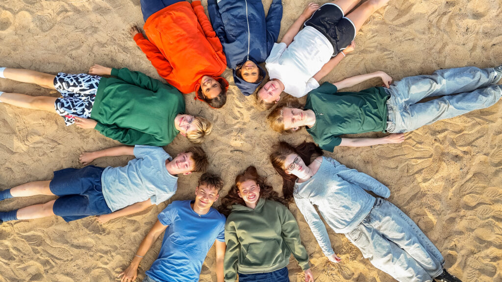 Nuoret makaavat ympyrän muodossa hiekkarannalla.